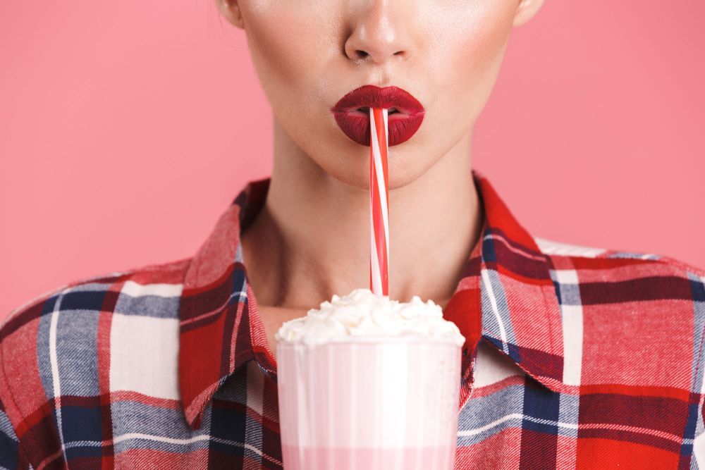 Eine Frau mit rotem Lippenstift trinkt einen Milchshake durch einen Strohhalm.